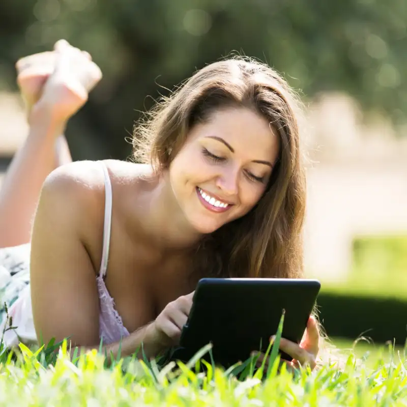 Junge Frau auf einer grünen Wiese tippt auf ihrem Tablet.