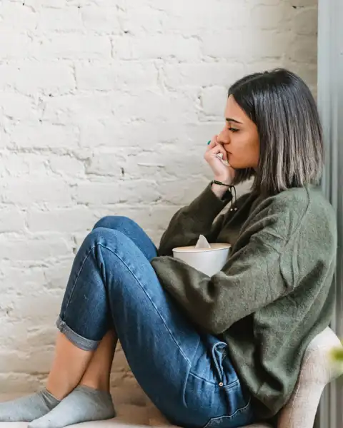 Eine traurige Frau sitzt seitlich auf einer Chaiselongue vor einer weissen, rustikalen Wand