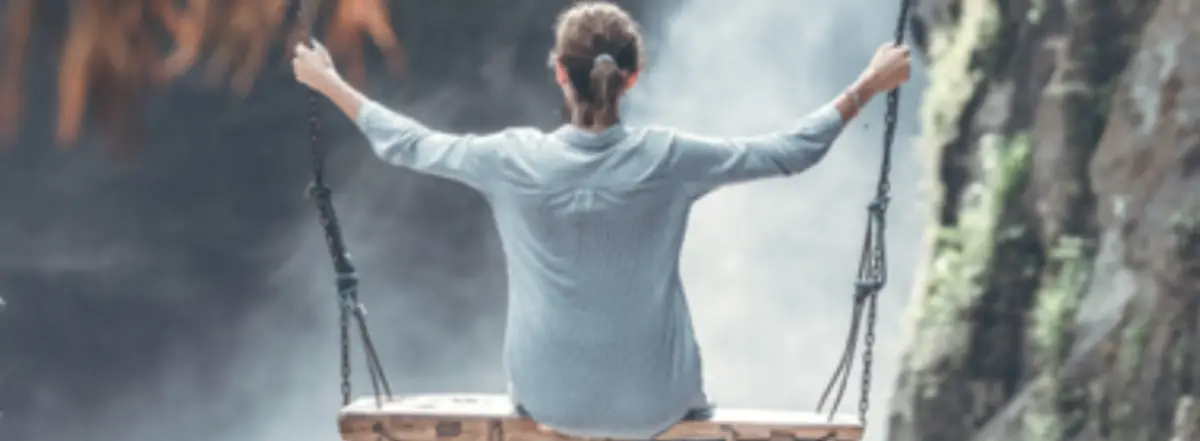 balance Eine Frau - ihr Rücken dem Betrachter zugewendet - sitzt auf einer Schaukel und betrachtet einen Wasserfall.