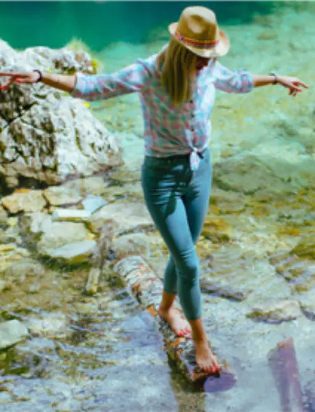 resilient Eine junge Frau balanciert auf einem Stück Baumstamm im seichten Wasser eines Baches.