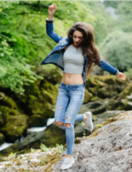 unabnhaengig Eine junge Frau in Jeanskleidung hüpft über Felsen durch die Natur