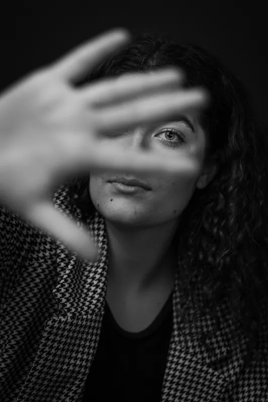 Eine Frau streckt Ihre Hand mit gspreizten Fingern vor ihrem Gesicht gegen die Kamera. Schwarz-Weiss Aufnahme.