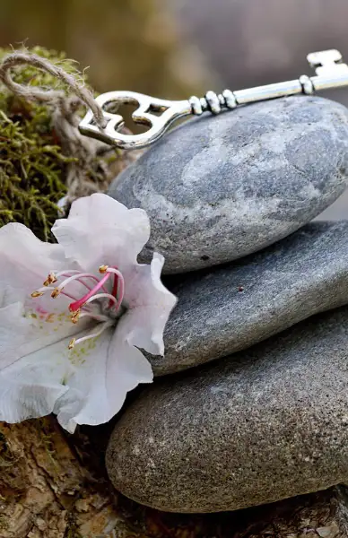 schluessel Stilleben mit Lilienblüte, altmodischem Schlüssel und Steinmännchen.