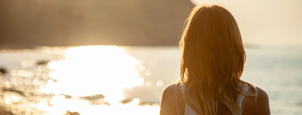 Frau blickt auf das im Sonnenuntergang glitzernde Meer.
